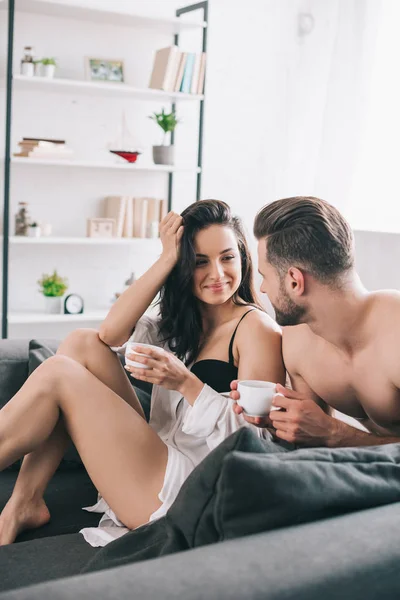 Sexy man and attractive woman in bra holding cups and looking at each other — Stock Photo