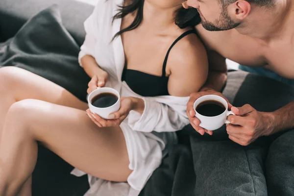 Обрізаний вид жінки в бюстгальтері і чоловік тримає чашки з кавою — стокове фото