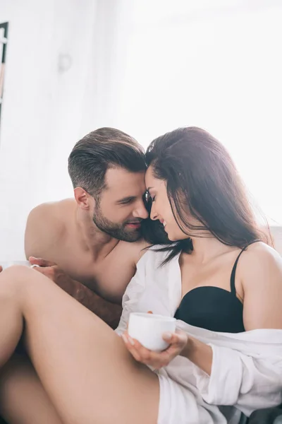 Handsome man and sexy woman in bra holding cup and kissing — Stock Photo