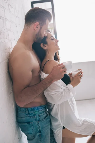 Side view of handsome man and sexy woman holding cups near wall — Stock Photo