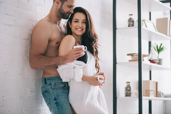 Bel homme et femme souriante en chemise tenant des tasses — Photo de stock