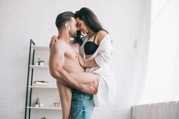Hombre guapo en jeans sosteniendo y besándose con mujer sexy en sujetador - foto de stock