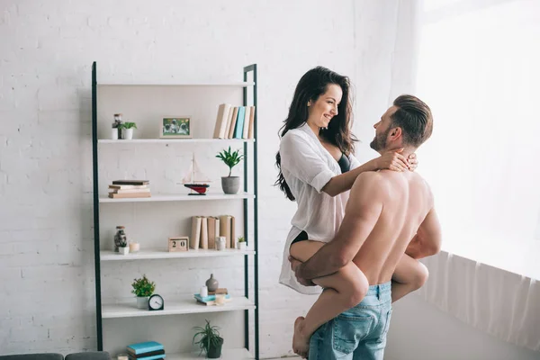 Homme musclé en jeans tenant et étreignant avec femme sexy en chemise — Photo de stock