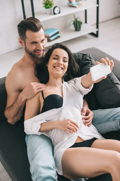 Hombre guapo y mujer sexy en camisa y sujetador sonriendo y tomando selfie - foto de stock