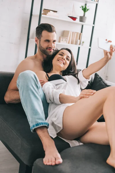 Guapo hombre y sexy mujer en camisa sonriendo y tomando selfie - foto de stock