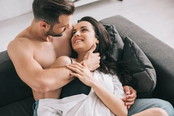 Handsome man and sexy woman in shirt lying on sofa and hugging — Stock Photo