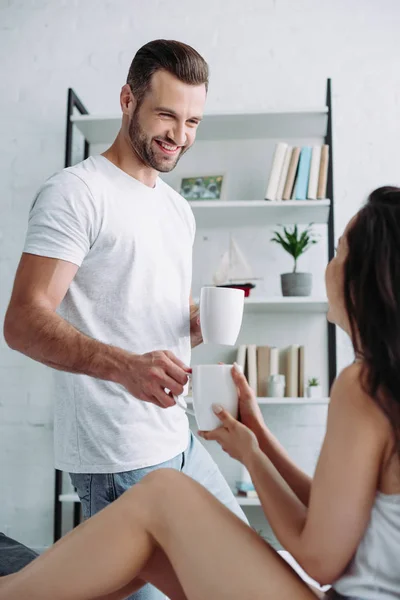 Handsome and smiling man giving cup with tea to brunette woman — Stock Photo