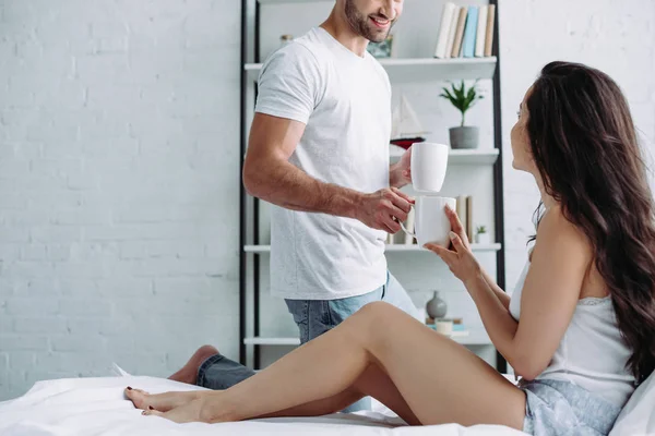 Cropped view of man in t-shirt giving cup with tea to brunette woman — Stock Photo