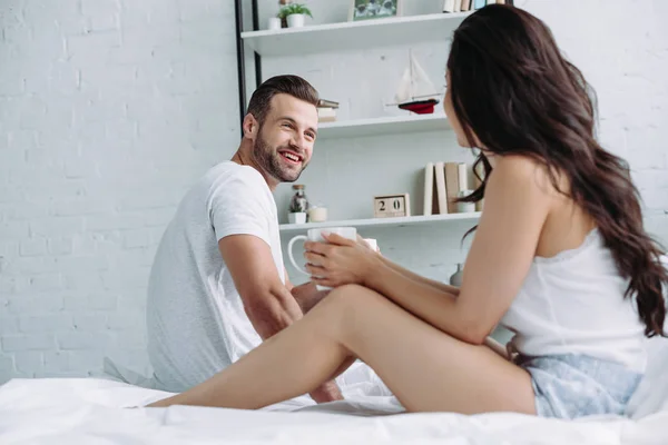 Hombre guapo y sonriente hablando con mujer morena en apartamento - foto de stock