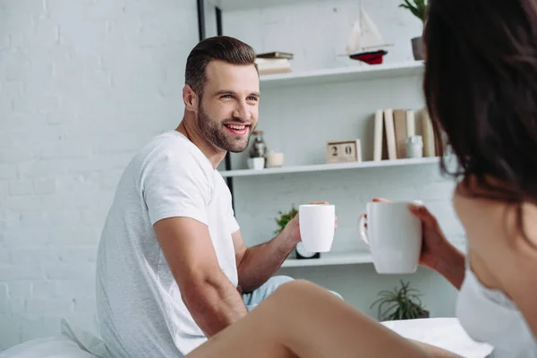 Guapo y sonriente hombre y mujer morena mirándose y sosteniendo copas - foto de stock