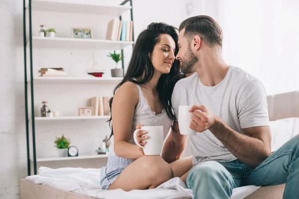 Attractive and brunette woman with closed eyes and man with cups kissing — Stock Photo
