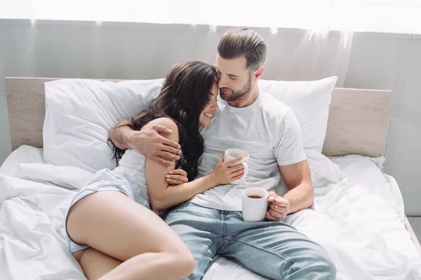 Attractive and brunette woman and man lying on bed and hugging — Stock Photo