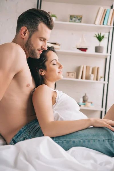 Side view of handsome man and beautiful woman sitting on bed — Stock Photo