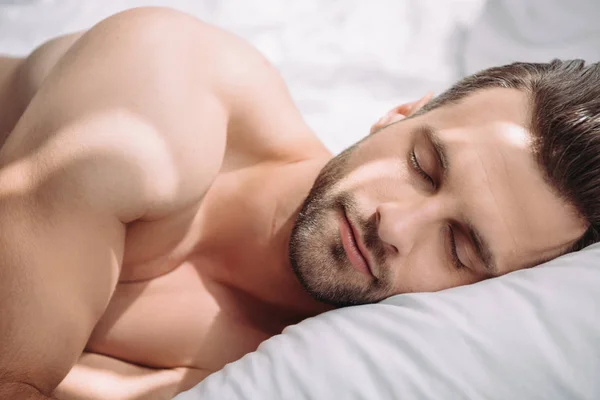 Hombre guapo y sin camisa con los ojos cerrados durmiendo en la cama - foto de stock