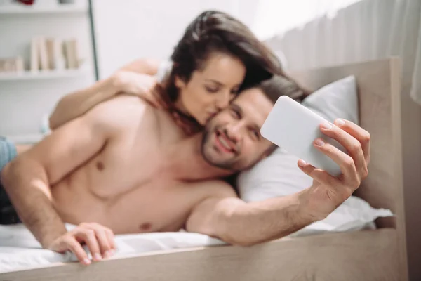 Selective focus of beautiful woman kissing handsome man and taking selfie — Stock Photo