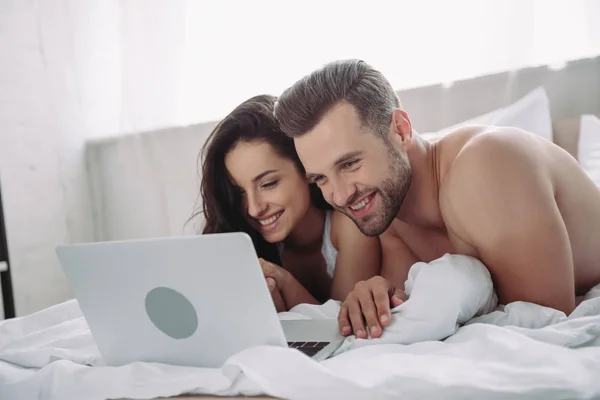Schöne Frau und schöner Mann auf dem Bett liegend und mit Laptop — Stockfoto
