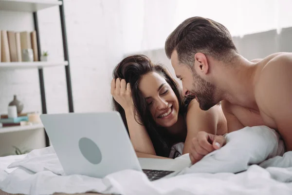 Belle femme et bel homme couché sur le lit avec ordinateur portable — Photo de stock