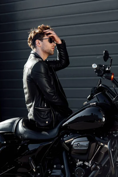 Joven guapo sentado en la motocicleta y reajustar el cabello - foto de stock