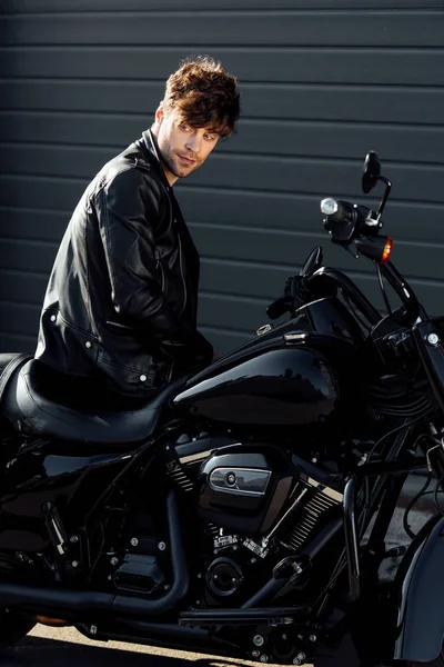 Young motorcyclist in black leather jacket sitting on motorcycle — Stock Photo