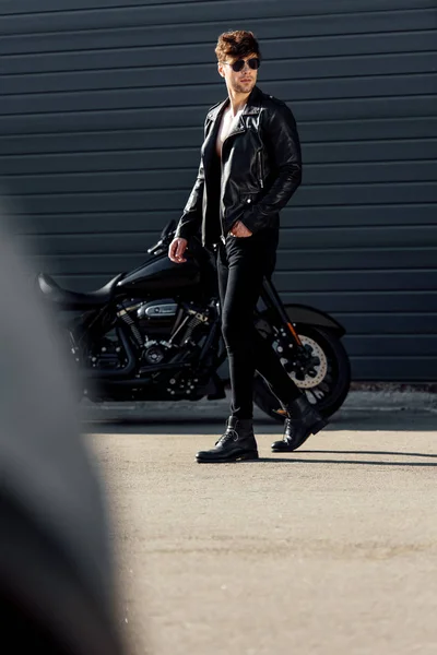 Вибірковий фокус молодого чоловіка, що стоїть зовні біля чорного мотоцикла — стокове фото