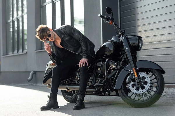 Hombre guapo sentado en moto negro y mirando a la cámara - foto de stock