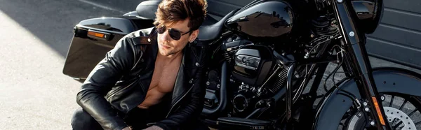 Panoramaaufnahme eines jungen Mannes in Brille und Lederjacke, der neben Motorrad sitzt — Stockfoto