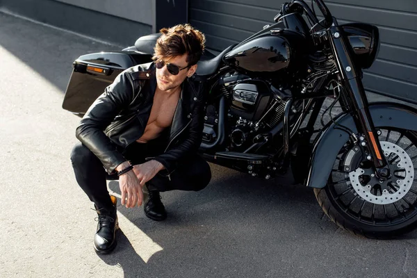 Мускулистый молодой человек сидит рядом с мотоциклом и смотрит в сторону — стоковое фото