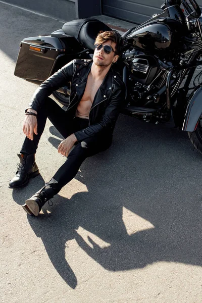 Jeune homme relaxant assis sur le sol près de moto noire — Photo de stock