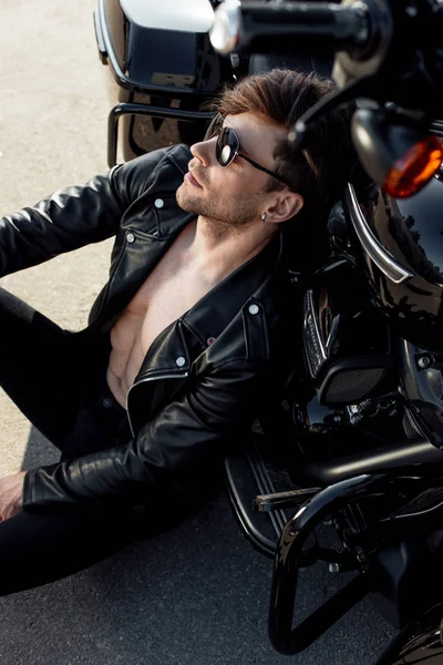 Muscular handsome man sitting on ground and leaning on motorcycle — Stock Photo