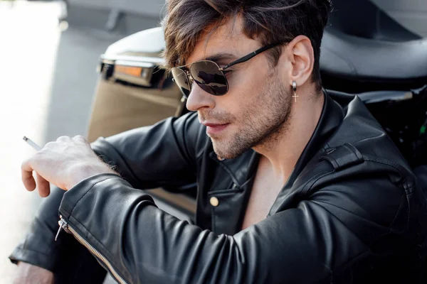 Young motorcyclist in leather jacket smoking while sitting near motorcycle — Stock Photo