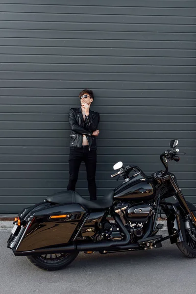 Full length view of young man smoking cigarette while leaning on wall and standing near motorcycle — Stock Photo