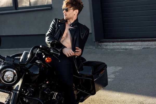 Без рубашки молодой человек в кожаной куртке отдыхает на черном мотоцикле — стоковое фото