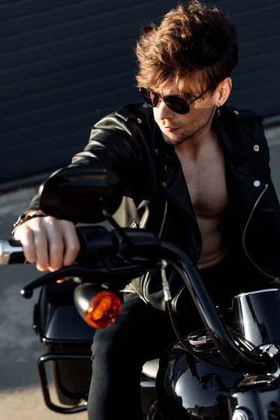 Jeune homme assis sur la moto dans la lumière du soleil, tenant la poignée et regardant loin — Photo de stock