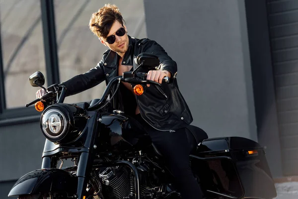 Motocycliste en veste en cuir assis sur la moto et regardant ailleurs — Photo de stock