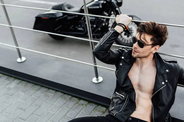 Selective focus of man with muscular torso sitting on ground and holding metal fence — Stock Photo