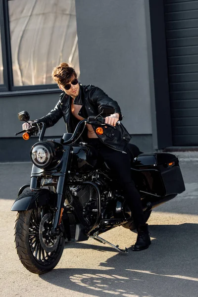 Full length view of motorcyclist in black leather jacket and sunglasses sitting on motorcycle — Stock Photo
