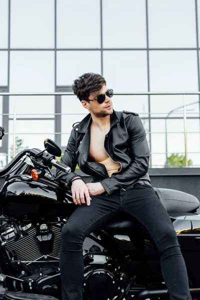 Vista frontal del joven apoyado en una motocicleta negra y mirando hacia otro lado - foto de stock