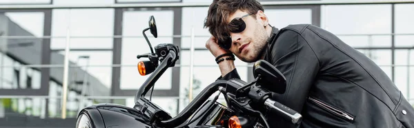 Panoramic shot of handsome young man in leather jacket resting while sitting on motorcycle — Stock Photo