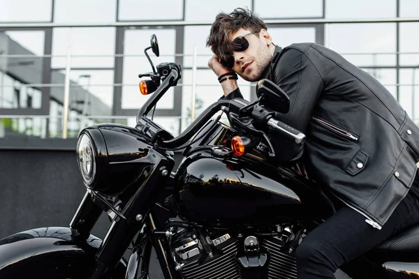 Schöner junger Mann in Lederjacke, während er auf einem neuen schwarzen Motorrad sitzt — Stockfoto