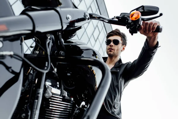 Low angle view of handle with orange headlight and man in leather jacket sitting on motorcycle — Stock Photo
