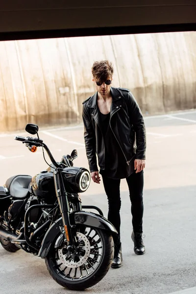 Handsome young man walking to garage to black motorcycle — Stock Photo