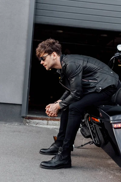 Vue latérale du bel homme en veste en cuir assis sur une moto noire — Stock Photo