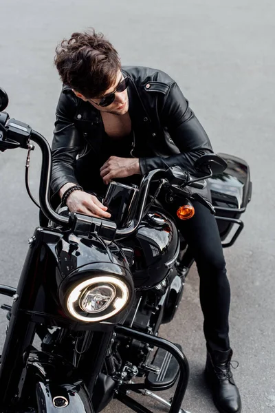 Vista de ángulo alto de hombre joven en chaqueta de cuero sentado en motocicleta - foto de stock
