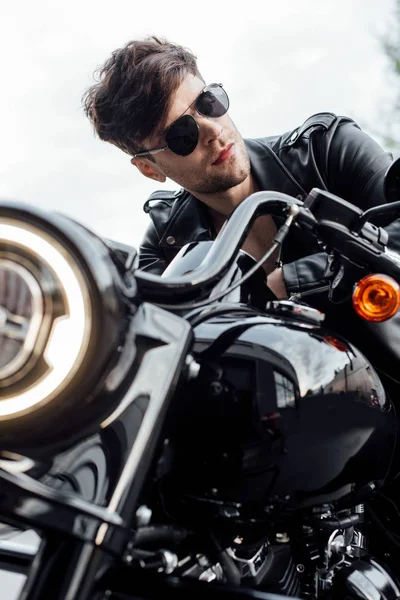 Selective focus of handsome motorcyclist in leather jacket looking away while sitting on motorcycle — Stock Photo