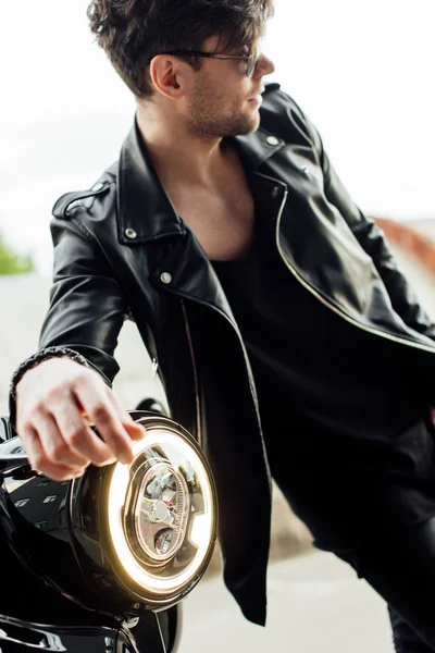 Enfoque selectivo de la lámpara de luz de la motocicleta y el hombre guapo en gafas de sol de pie cerca de la motocicleta - foto de stock