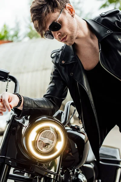 Hombre guapo en chaqueta de cuero apoyado en el manillar de la motocicleta - foto de stock