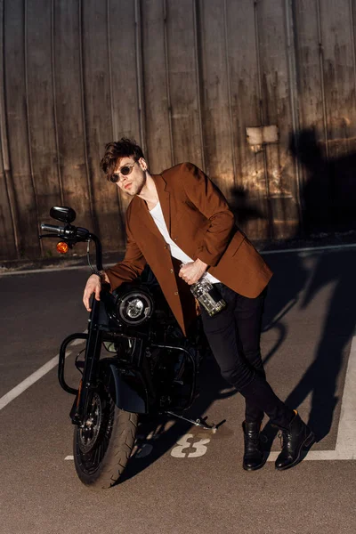 Ganzkörperansicht eines Mannes im Anzug, der sich auf ein Motorrad lehnt und eine Alkoholflasche hält — Stockfoto