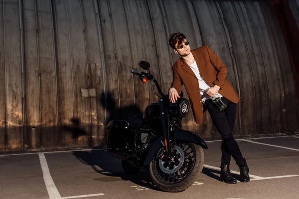 Ganzkörperansicht eines Mannes, der an einem hellen Ort steht und sich auf ein Motorrad stützt — Stockfoto