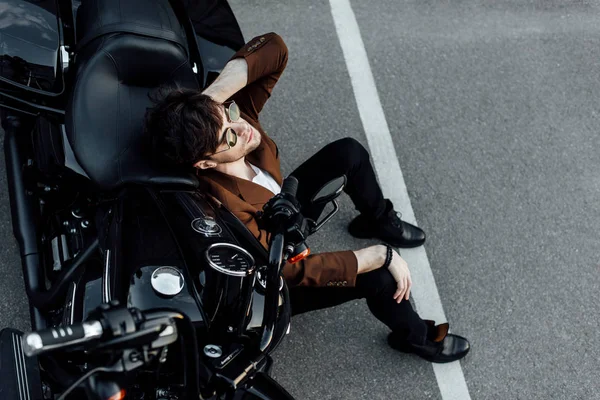 Vue de dessus de l'homme en lunettes de soleil et costume assis sur le sol près de la moto — Photo de stock