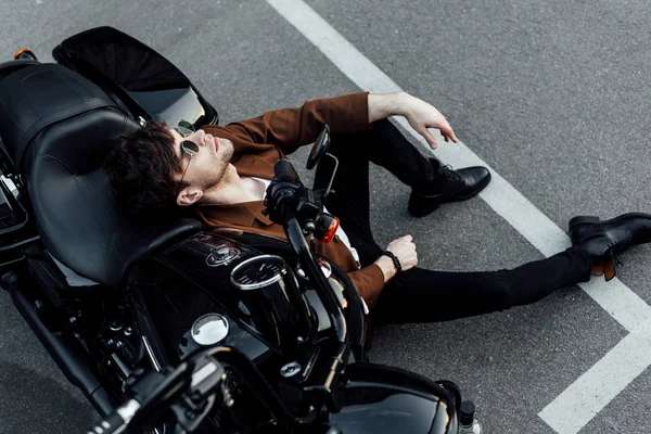 Top view of man resting while leaning on balck motorcycle and sitting on alphalt — Stock Photo